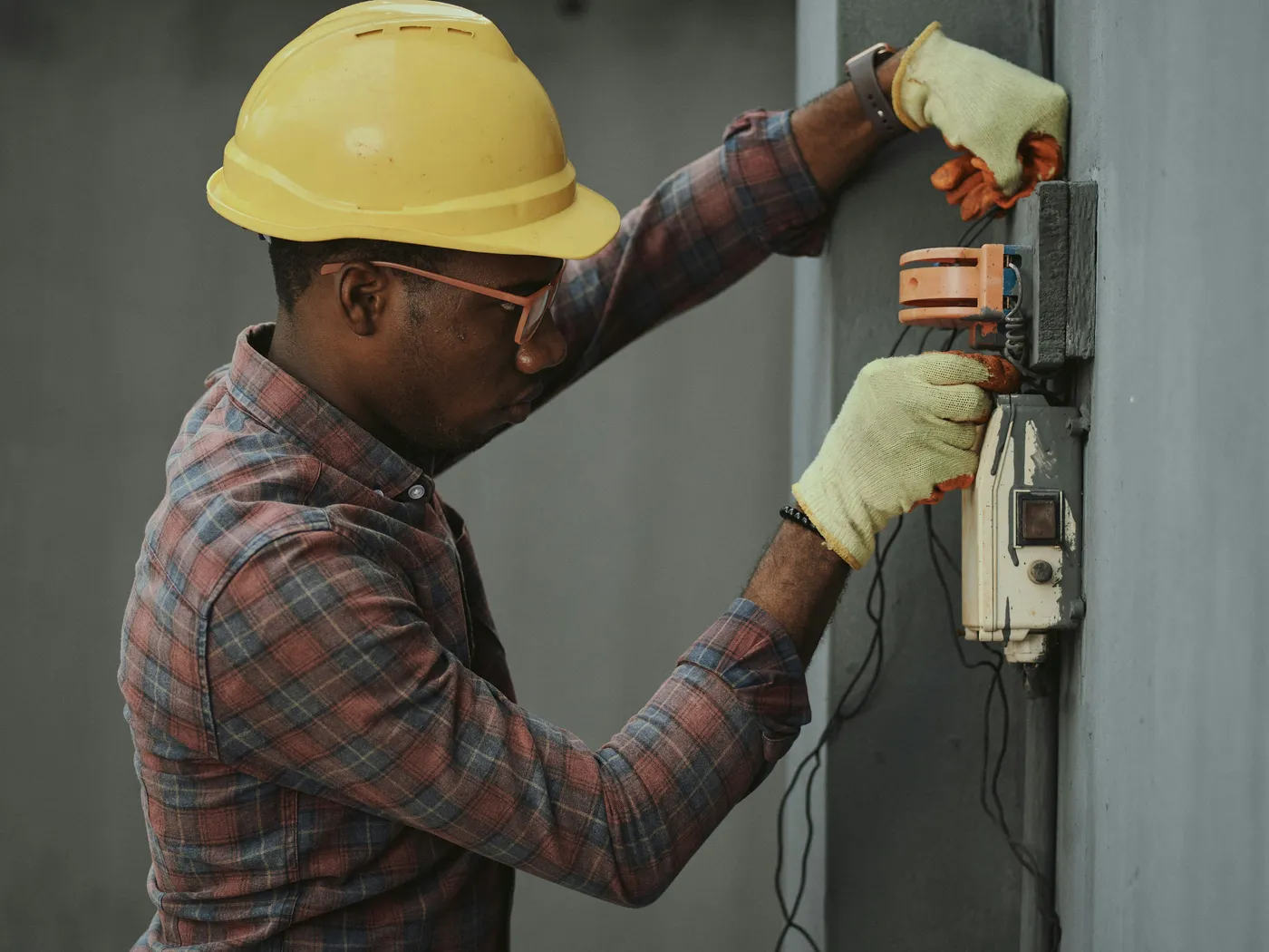 An electrician in a hard hat wiring a meter box on an outside wall